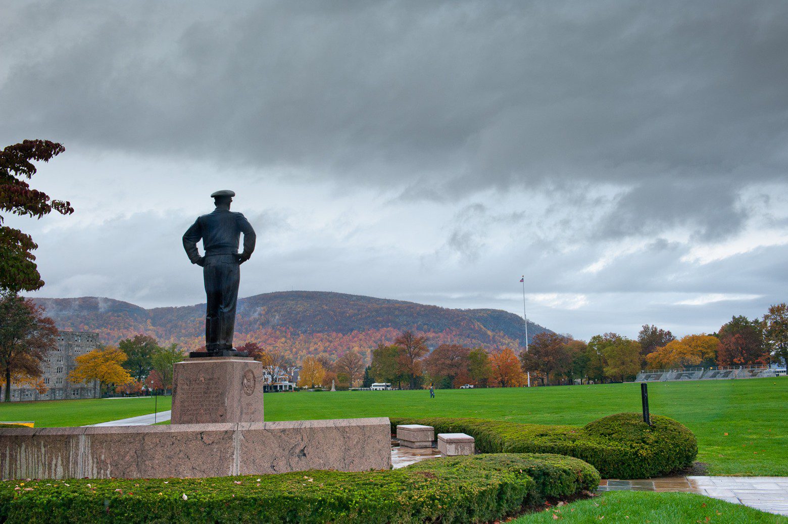 A statue of a man standing with hands on hips against a cloudy sky.