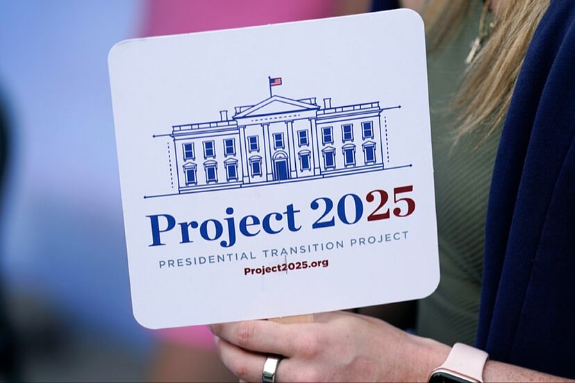 A hand holding a coaster with a White House illustration and text 'Project 2025'.