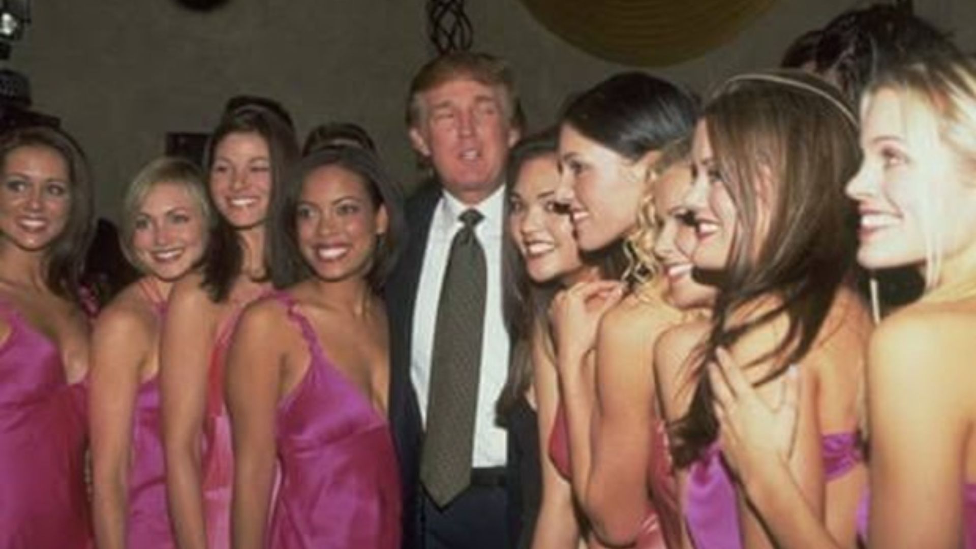 Donald Trump posing with six women in glamorous dresses.