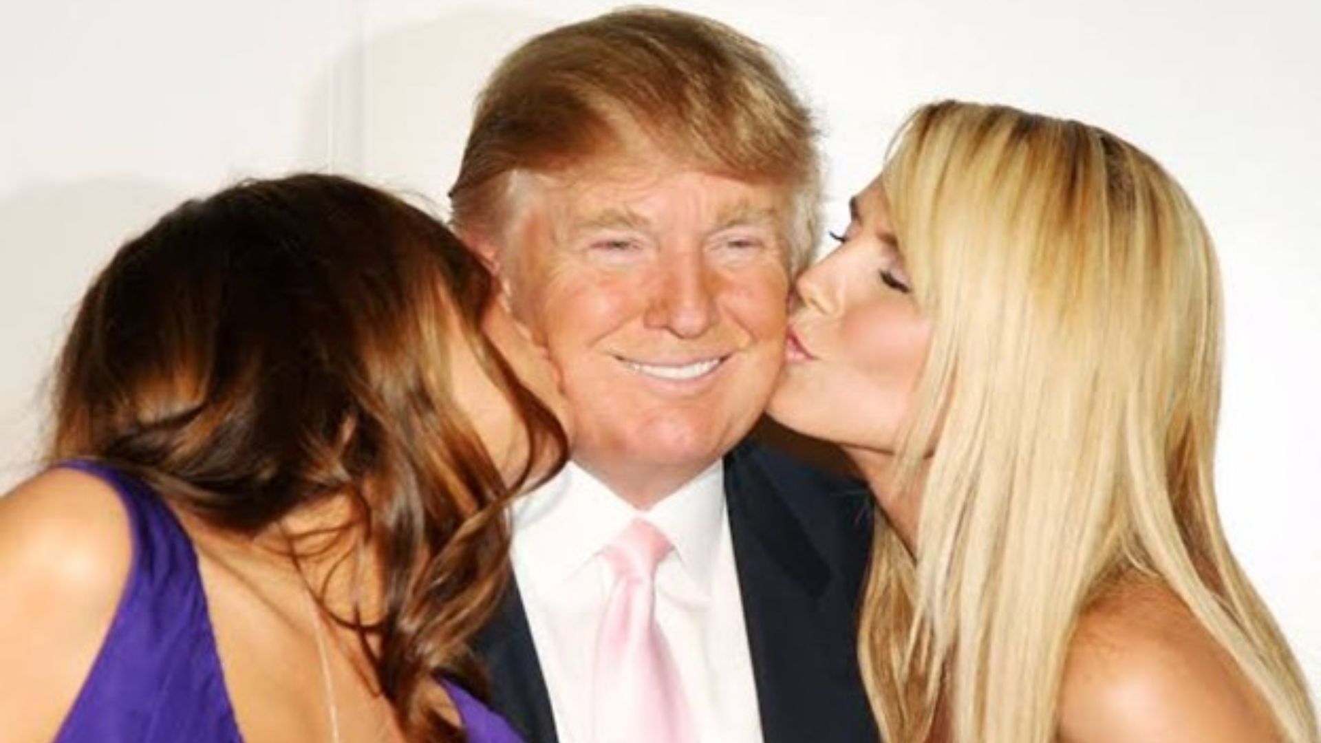 A man smiling with two women kissing his cheeks.
