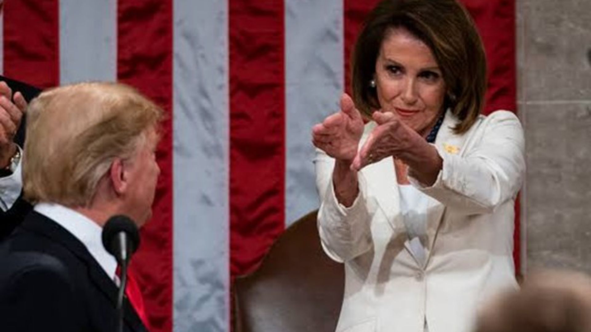 A woman in white gestures with her thumb down while a man looks on.