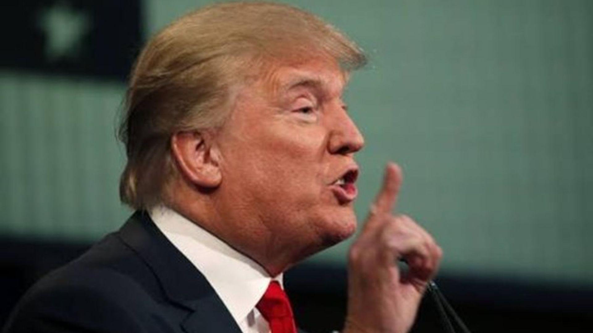 A man with blonde hair speaking emphatically with finger raised.
